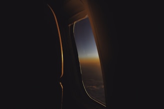 A modern airplane window view with a serene sky at sunrise, suggesting new horizons.