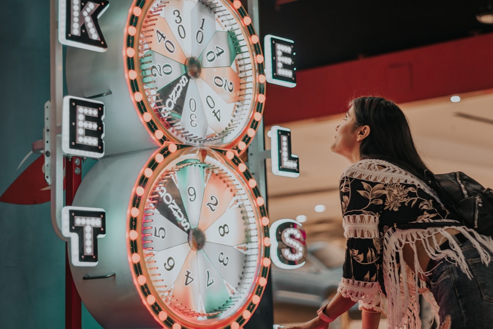 woman in black and white floral dress standing near analog wall clock