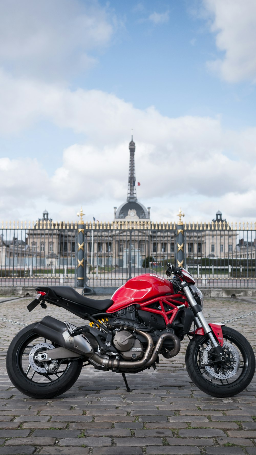 낮에는 흰색 콘크리트 건물 근처에 주차된 빨간색과 검은색 오토바이