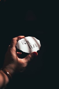 A hand holds a torn piece of paper with the words 'Spread hope not fear' written on it in a dark, moody setting.