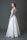 A bride wearing a long white lace and tulle gown with a fitted bodice and a flowing skirt. Her hair is styled elegantly, and she is accessorizing with large earrings and a bracelet. The background is a solid gray tone.