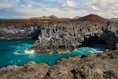 brown rocky mountain beside blue sea under blue sky during daytime
