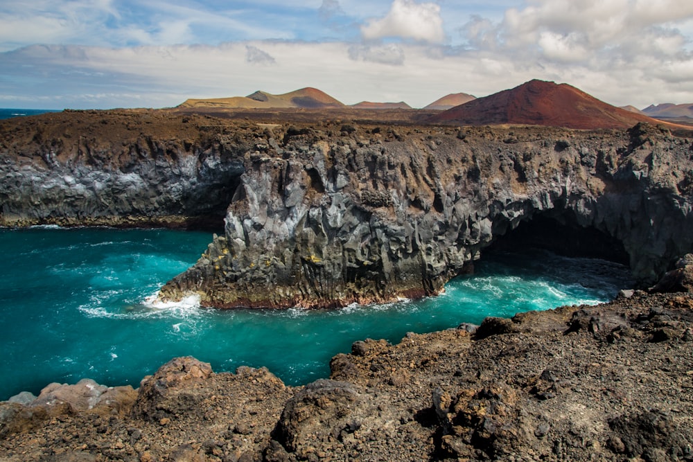 brown rocky mountain beside blue sea under blue sky during daytime