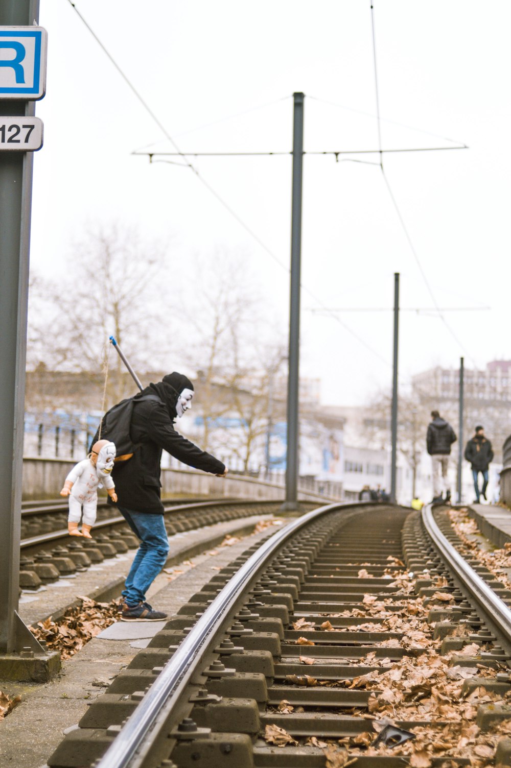 man in black jacket and blue denim jeans standing on train rail during daytime