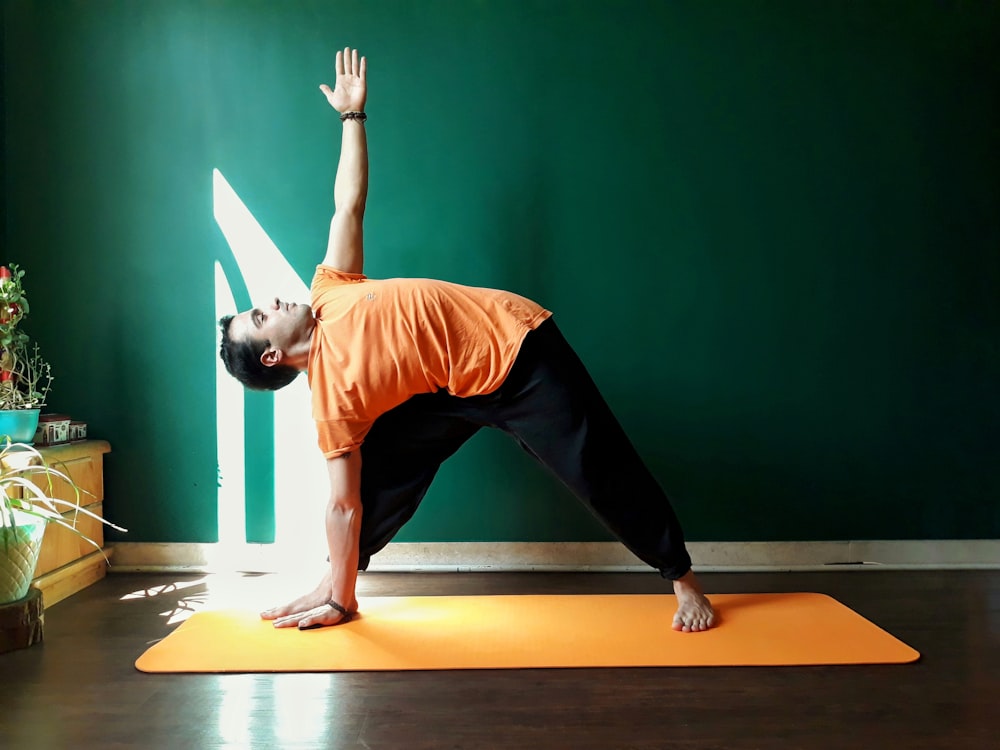 femme en débardeur orange et pantalon noir faisant du yoga