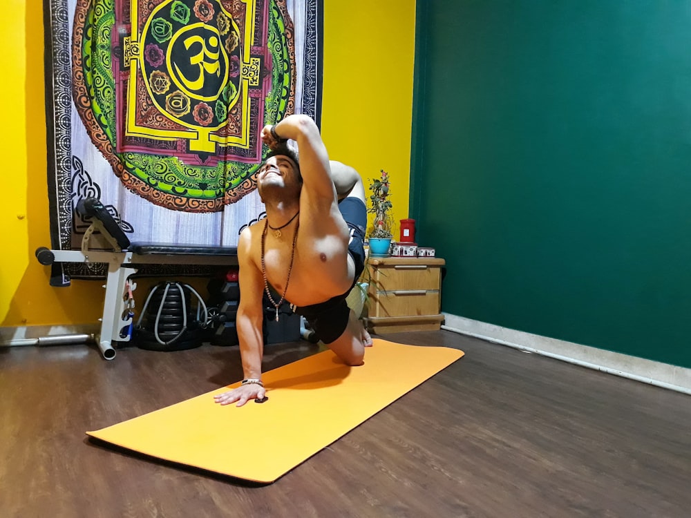 topless man in black shorts kneeling on yellow yoga mat