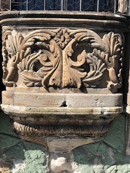 A detailed stone carving featuring intricate floral patterns and symmetrical designs, possibly part of an architectural structure. The carving includes ornate leaves and scrolls, highlighting skilled craftsmanship.