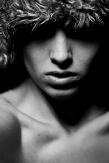 Moody black and white photo of a man with a solemn expression wearing a textured hat, with deep shadows around