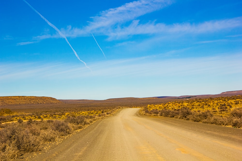 Camino de tierra marrón entre el campo de hierba verde bajo el cielo azul durante el día