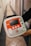 A person is holding a medical device, specifically an automated external defibrillator (AED), with a red accent and labeled 'iPAD'. The device has a screen, control buttons, and an on/off switch. The hallway setting in the background includes tiles on the floor.