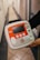 A person is holding a medical device, specifically an automated external defibrillator (AED), with a red accent and labeled 'iPAD'. The device has a screen, control buttons, and an on/off switch. The hallway setting in the background includes tiles on the floor.