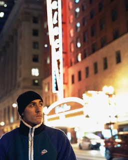 Nighttime street scene with a person wearing lumina apparel outerwear, city lights blurred in background.