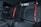 The image features the back seat of a car interior, showcasing black leather upholstery with red stitching and red seat belts. The design is sleek and modern, indicating a focus on style and comfort.
