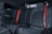 The image features the back seat of a car interior, showcasing black leather upholstery with red stitching and red seat belts. The design is sleek and modern, indicating a focus on style and comfort.