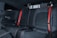 The image features the back seat of a car interior, showcasing black leather upholstery with red stitching and red seat belts. The design is sleek and modern, indicating a focus on style and comfort.