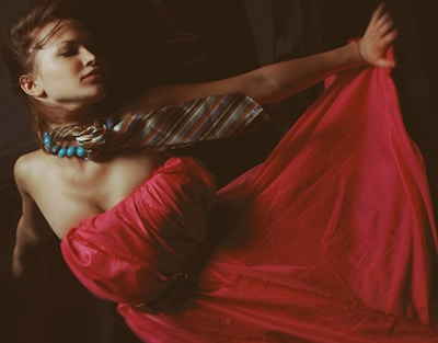 A person is dressed in a flowing red gown with a striped scarf and blue beaded necklace. The composition evokes a sense of elegance and movement.
