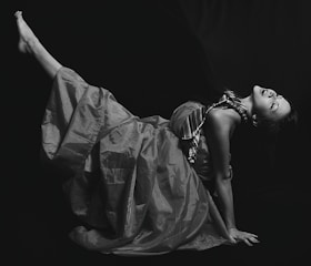 A striking black and white fashion portrait of a model wearing a flowing silk dress, set against a bright white background.