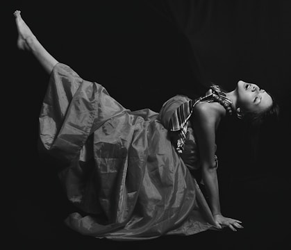 A striking black and white fashion portrait of a model wearing a flowing silk dress, set against a bright white background.