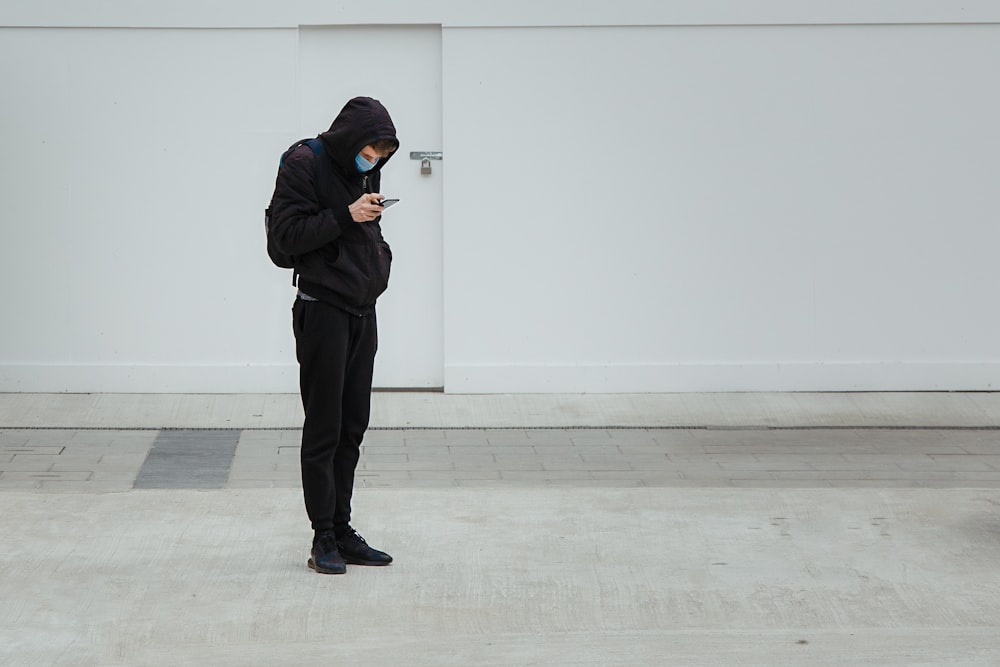 man in black hoodie and black pants standing near white wall