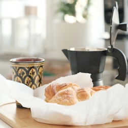 bread on white paper beside brown ceramic mug on brown wooden table