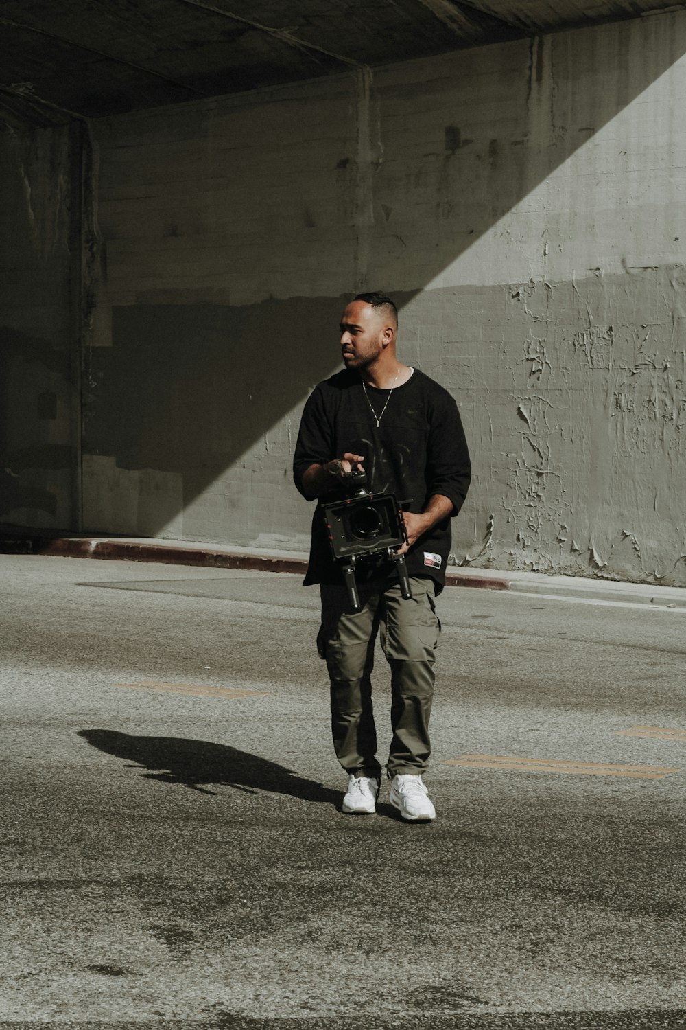 man in black crew neck t-shirt and brown pants standing on gray asphalt road during