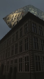 A modern building with a unique architectural design, featuring a glass structure with geometric patterns on top of an older style, multi-windowed base.