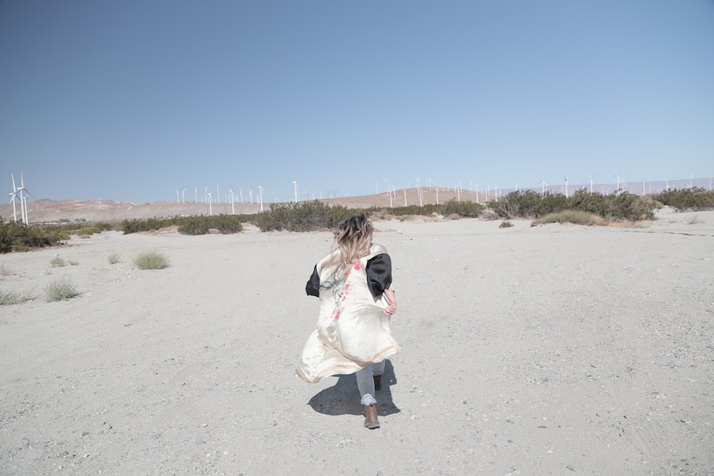 woman in white jacket walking on gray sand during daytime