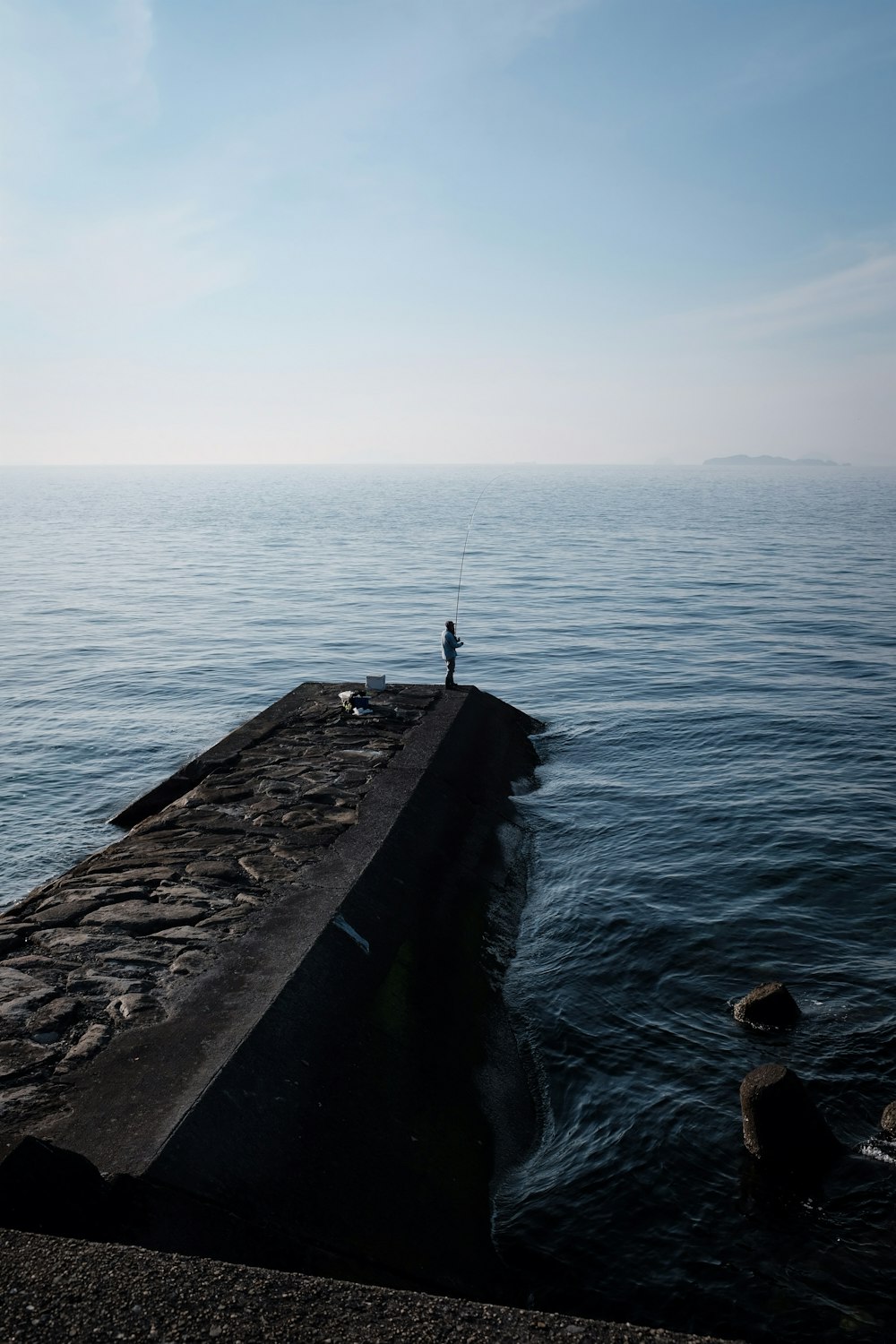 person standing on concrete dock near body of water during daytime