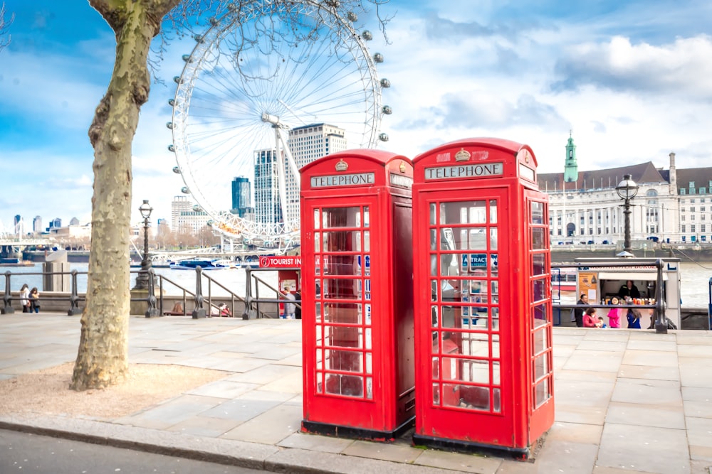 Cabina telefonica rossa vicino alla ruota panoramica sotto il cielo nuvoloso soleggiato blu e bianco durante il giorno