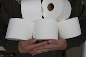 Several white toilet paper rolls are being held in someone's hands, with a focus on the texture and embossing of the paper.