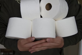 Several white toilet paper rolls are being held in someone's hands, with a focus on the texture and embossing of the paper.