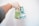A hand wearing a glove is holding Canadian banknotes against a plain white background. The banknotes are vibrant and colorful, primarily featuring a green and blue design, with the denominations clearly visible as 20 and 5.