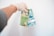 A hand wearing a glove is holding Canadian banknotes against a plain white background. The banknotes are vibrant and colorful, primarily featuring a green and blue design, with the denominations clearly visible as 20 and 5.