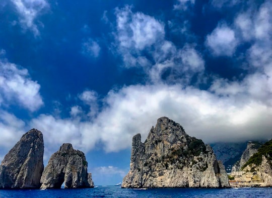 gray rock formation on sea under blue sky and white clouds during daytime in Capri Italy