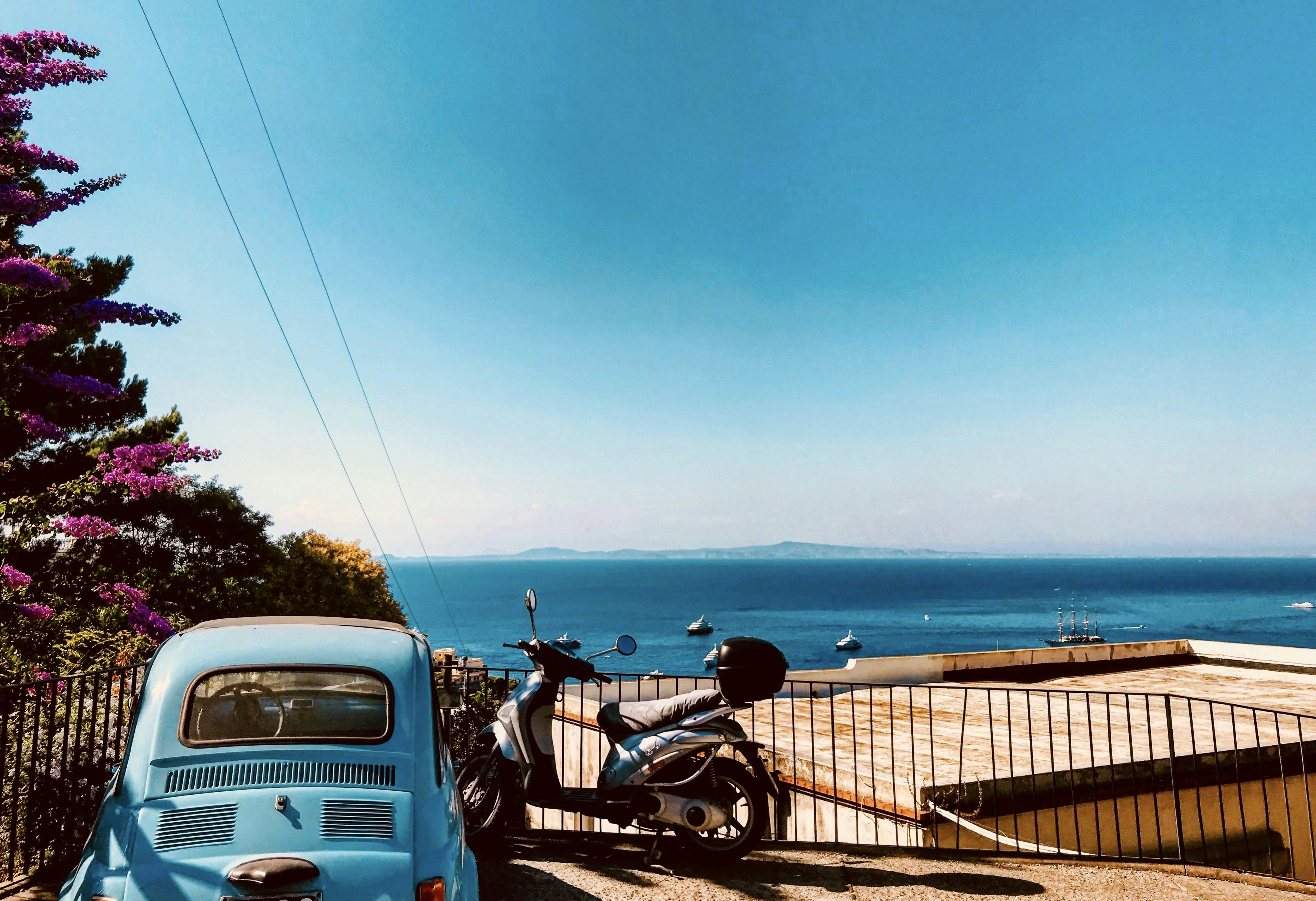 homme en veste noire conduisant une moto près d’une voiture blanche pendant la journée