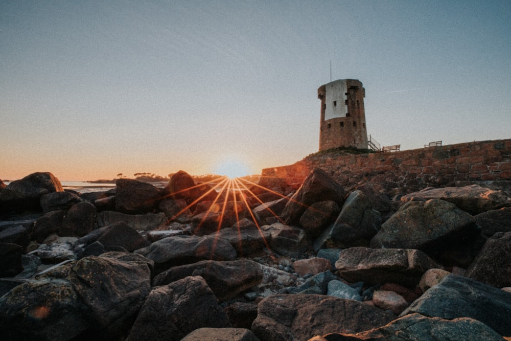 white concrete lighthouse on rocky shore during sunset