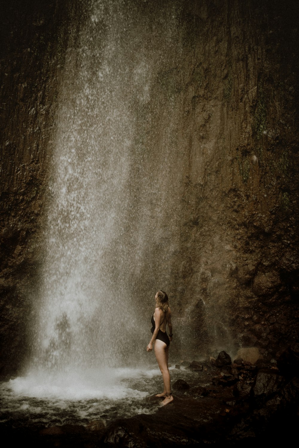 woman in black bikini sitting on rock near water falls during daytime