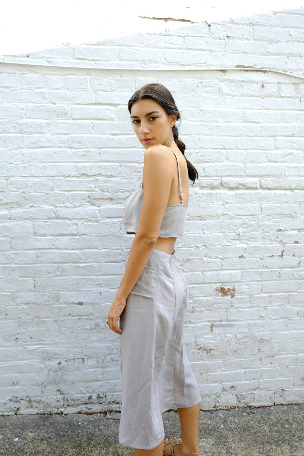 woman in white tank top and white pants standing beside brick wall