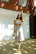woman in white spaghetti strap dress wearing sunglasses standing near white wall during daytime
