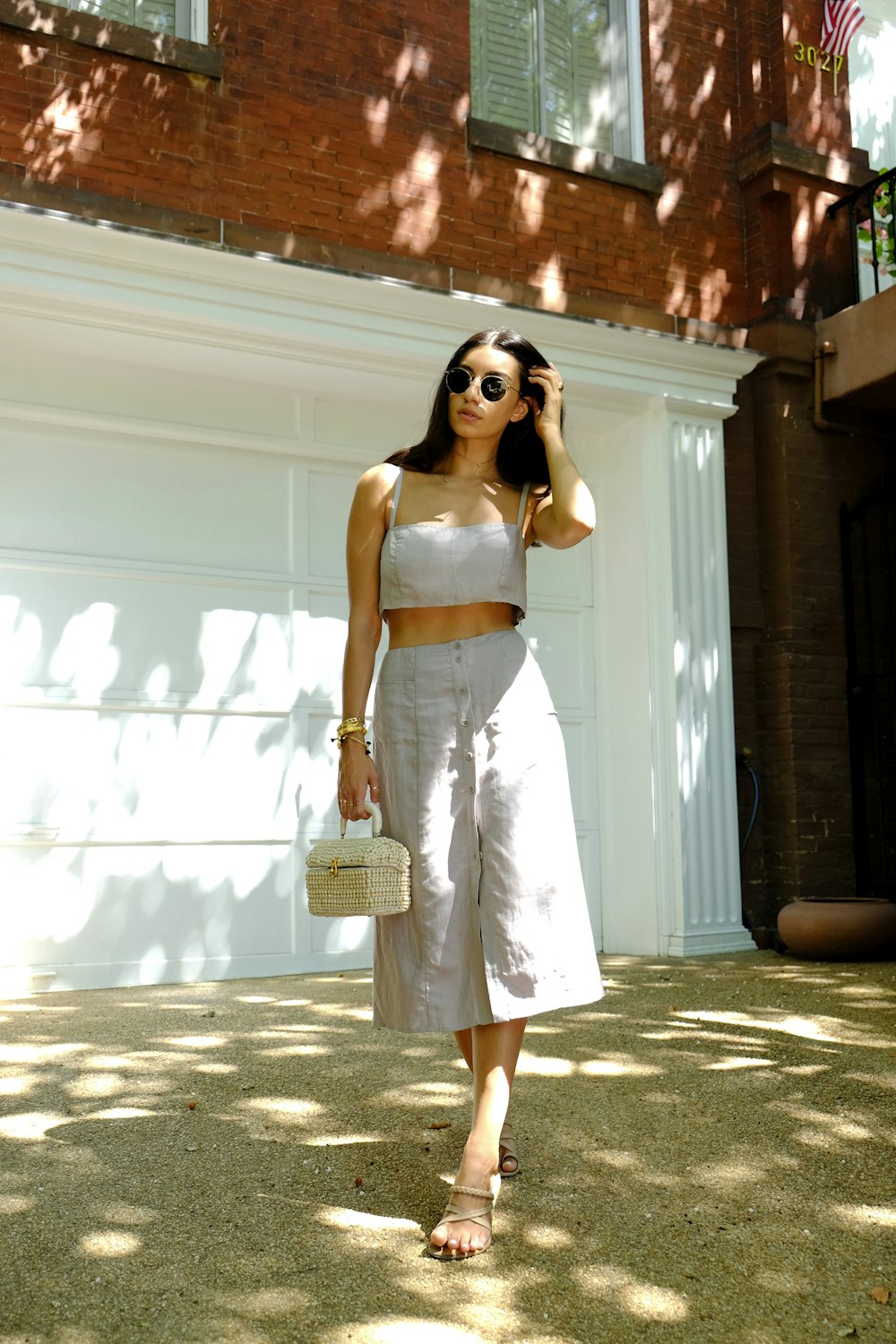 Femme en robe blanche à bretelles spaghetti portant des lunettes de soleil debout près d’un mur blanc pendant la journée