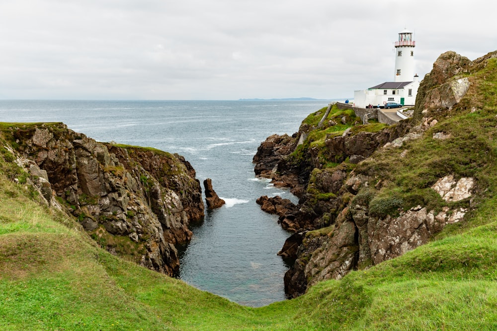 Phare blanc sur une formation rocheuse brune à côté d’un plan d’eau pendant la journée