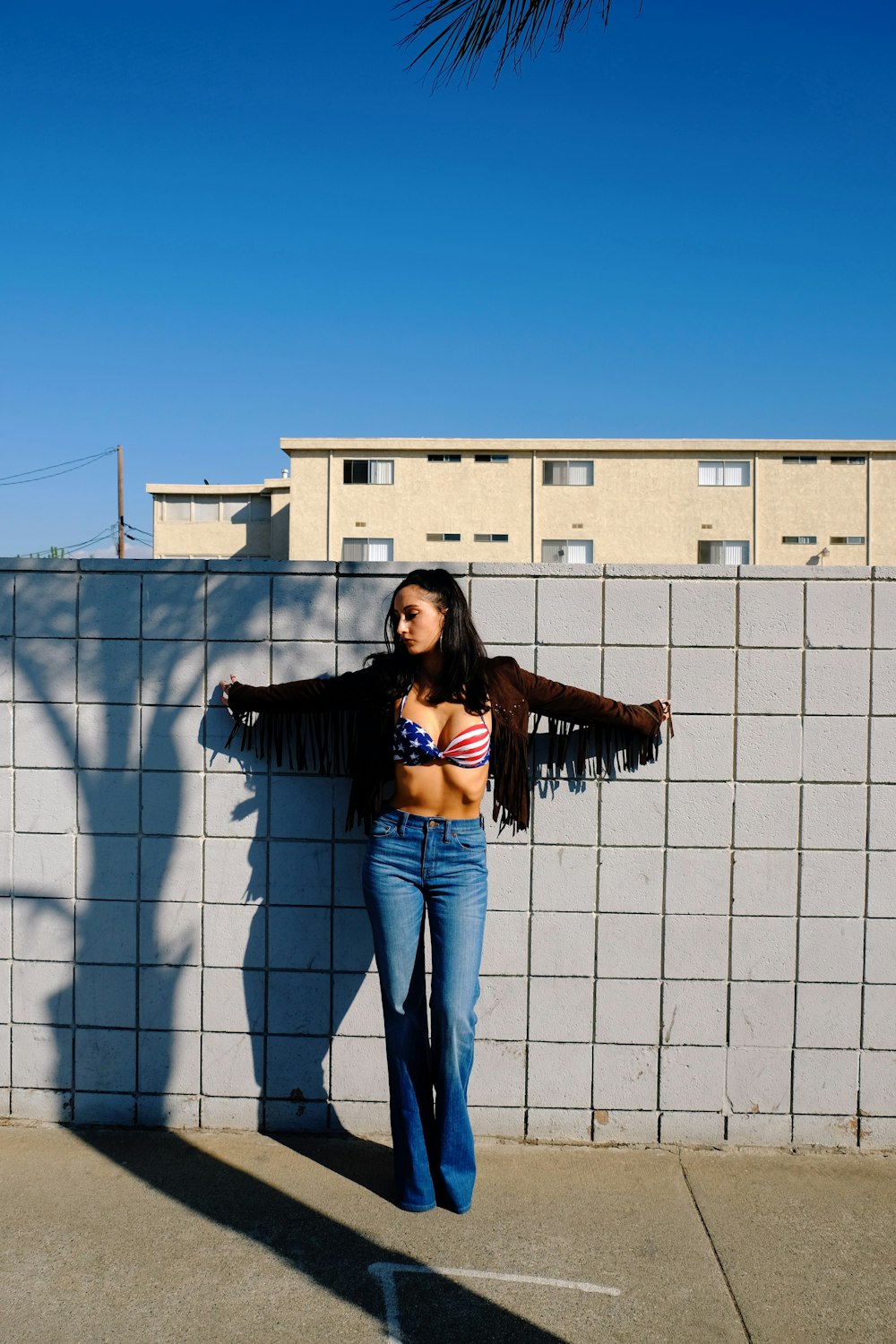 woman in blue denim jeans standing beside white concrete building during daytime