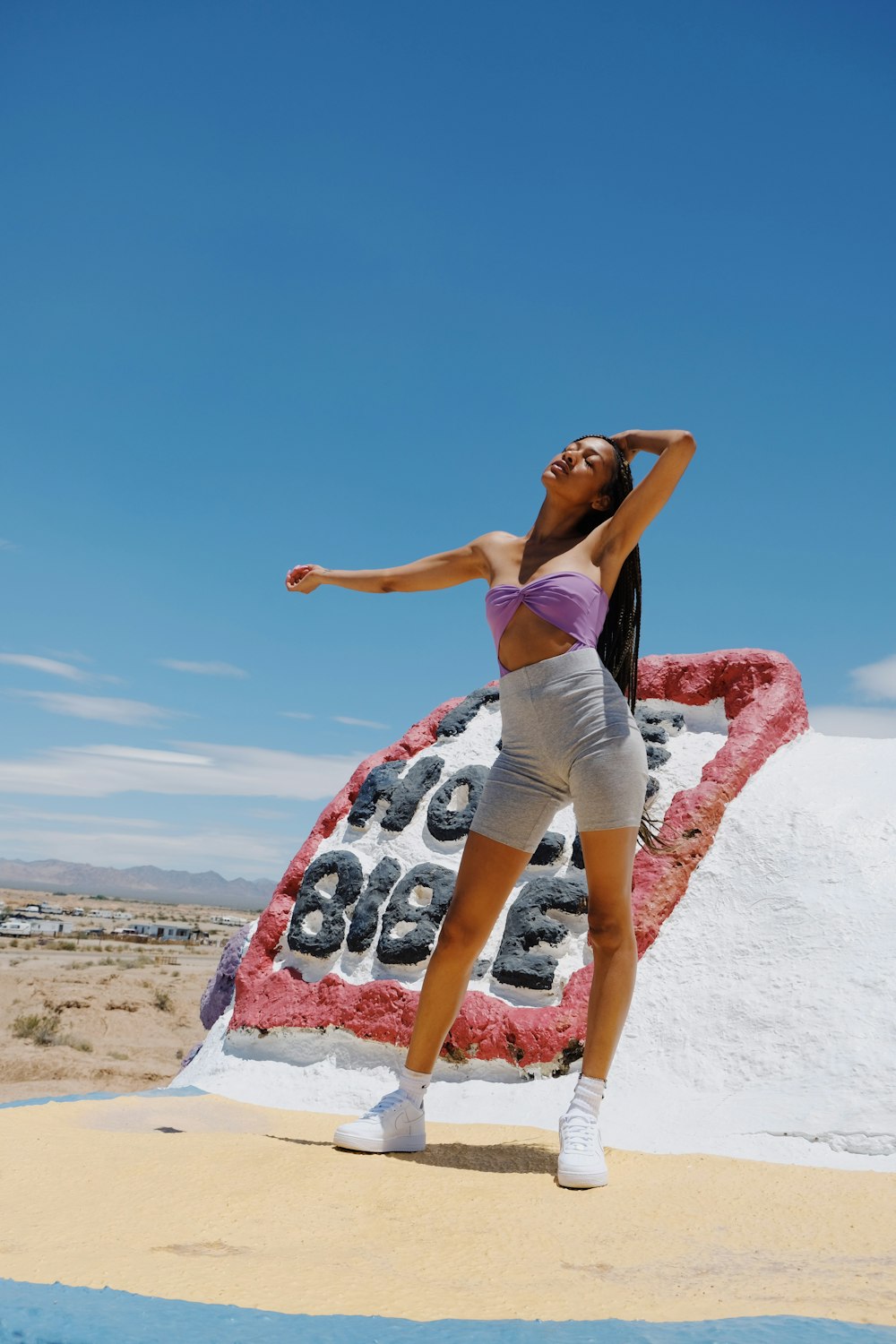 Mujer con camiseta sin mangas morada y pantalones cortos blancos haciendo yoga en la playa durante el día