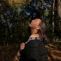 A joyful person wearing a Seekers Compass t-shirt, standing in a sunlit forest clearing