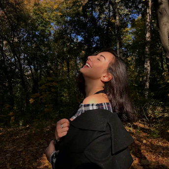 A joyful person wearing a Seekers Compass t-shirt, standing in a sunlit forest clearing
