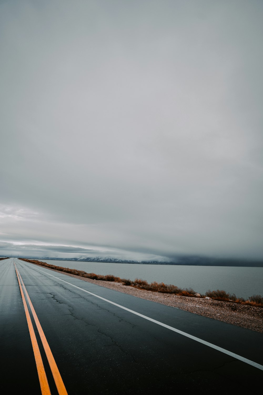 gray concrete road near body of water under white clouds during daytime