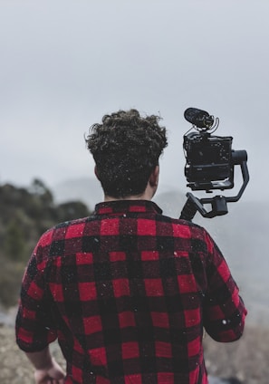 man in red and black plaid shirt holding black dslr camera