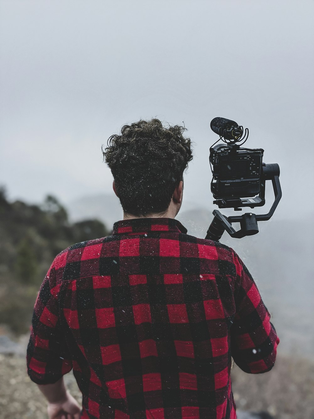 man in red and black plaid shirt holding black dslr camera