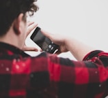 man in red and white checked shirt holding black smartphone