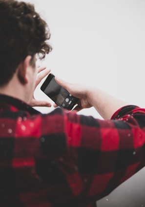 man in red and white checked shirt holding black smartphone